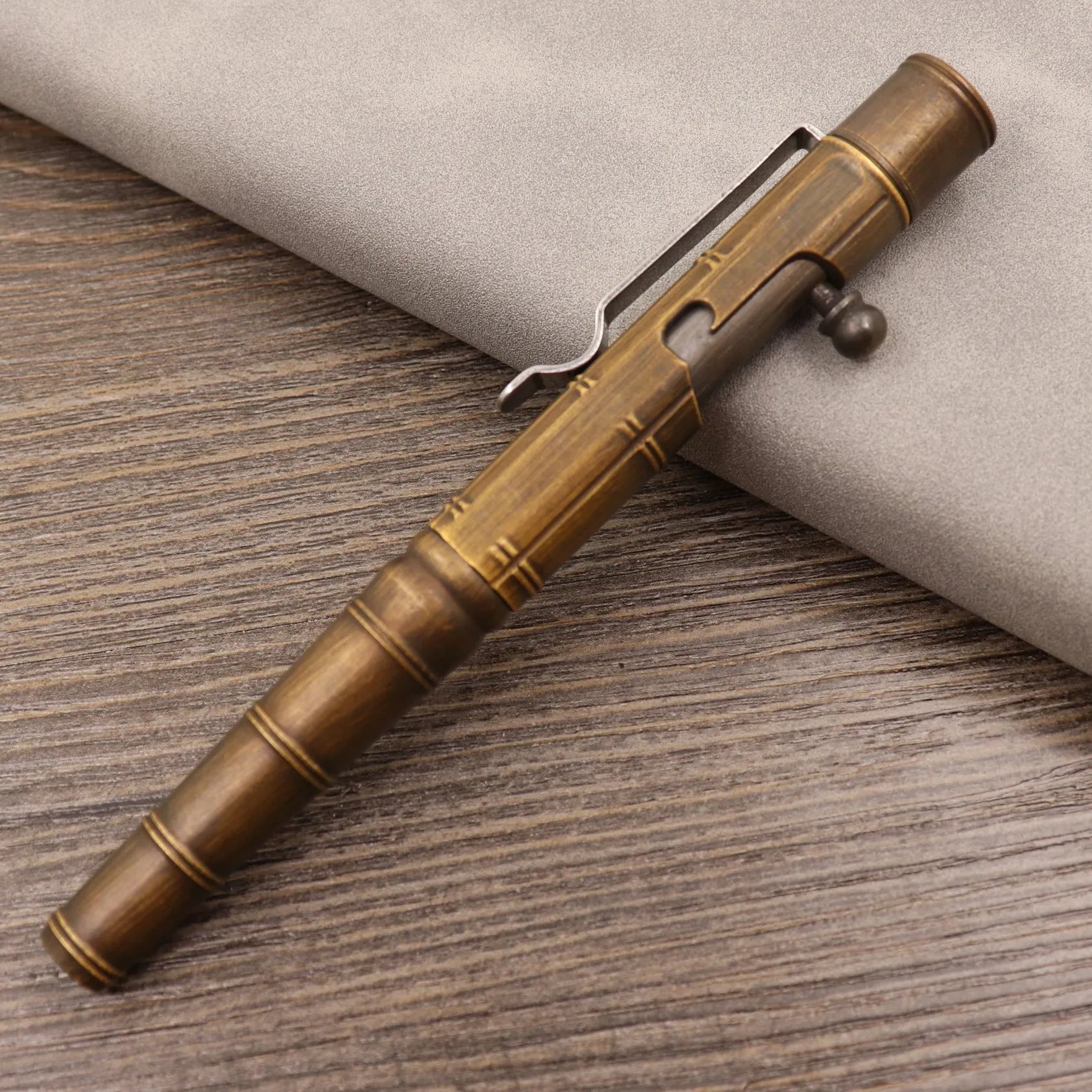 Brass bolt-action tactical pen in a retro copper finish, showing press mechanism and textured barrel.