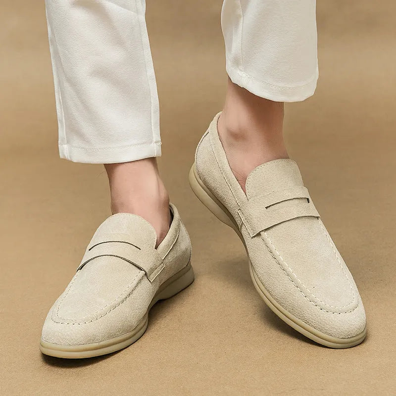 Men's brown leather slip-on casual shoes with round toe and rubber sole on a wooden floor.