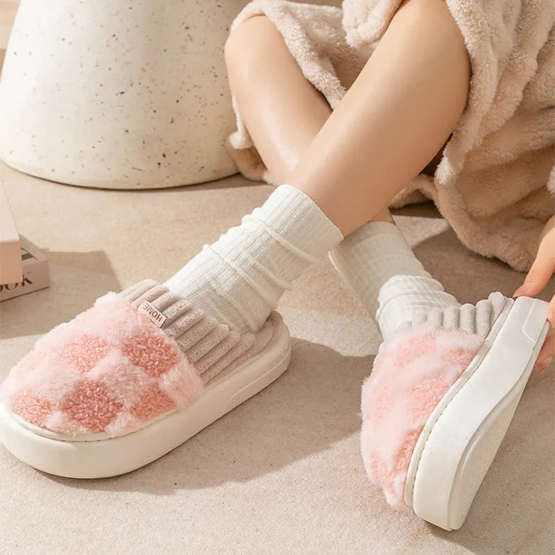 Women's plaid patterned coral velvet indoor slippers with a thick soft sole on a wooden floor.