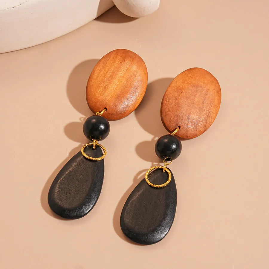 Handcrafted brown and black wooden elliptical earrings with silver needle detail on a retro style background.
