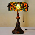 Tiffany style table lamp with coloured stained glass shade and resin base on a desk.