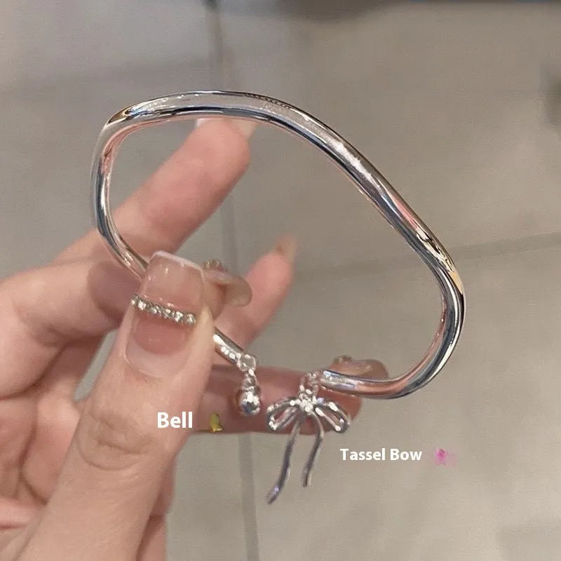 Silver adjustable bracelet with a detailed bow bell opening charm on a wrist.