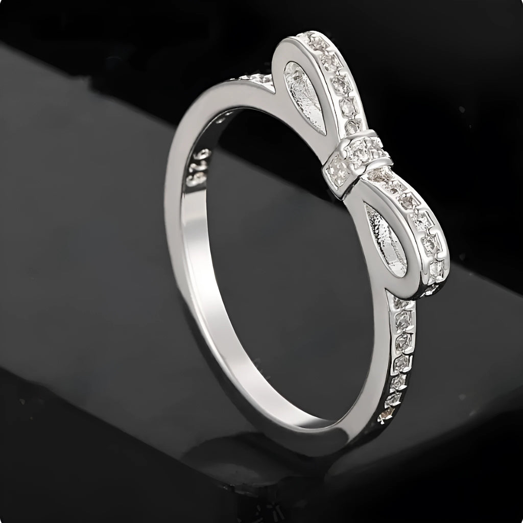 Silver-coloured bow-shaped ring with sparkling zircon crystal stones on a finger.