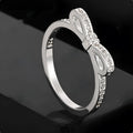 Silver-coloured bow-shaped ring with sparkling zircon crystal stones on a finger.