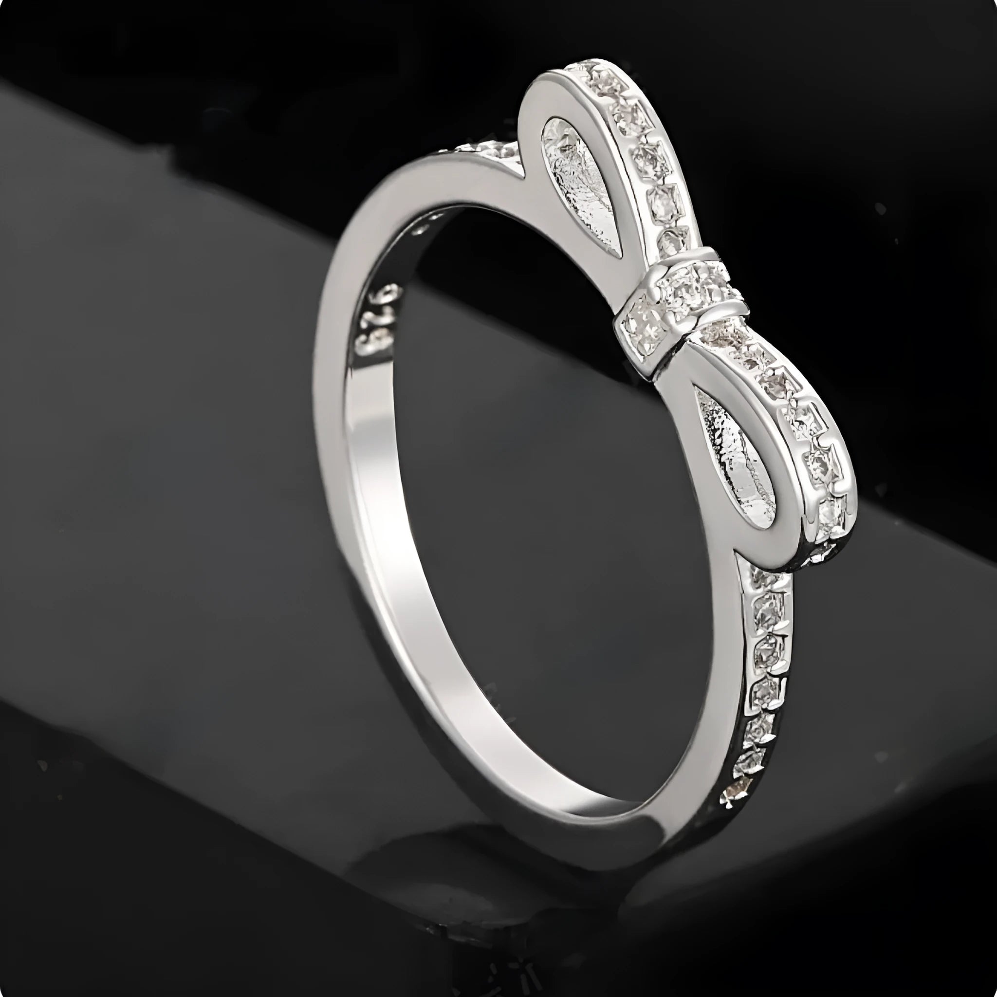 Silver-coloured bow-shaped ring with sparkling zircon crystal stones on a finger.