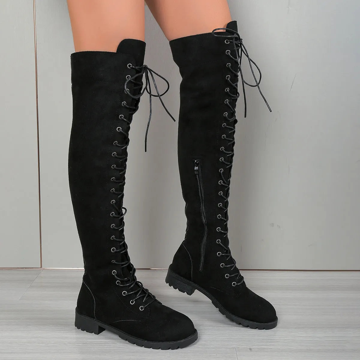 Black lace-up over-the-knee boots with a flat rubber sole and decorative stitching on the faux leather upper