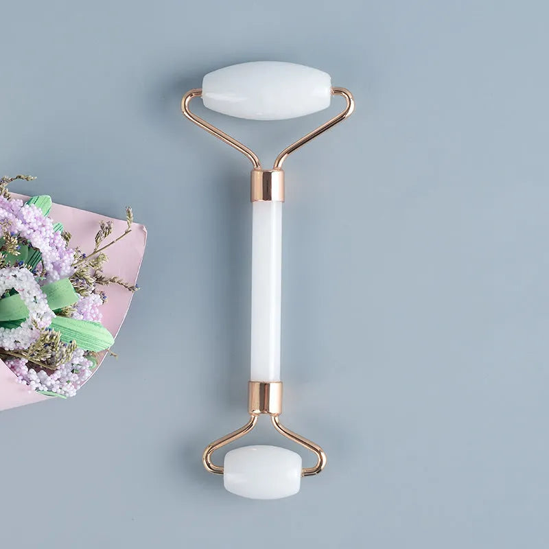 White jade double-headed facial roller and scraping board set on a plain surface.