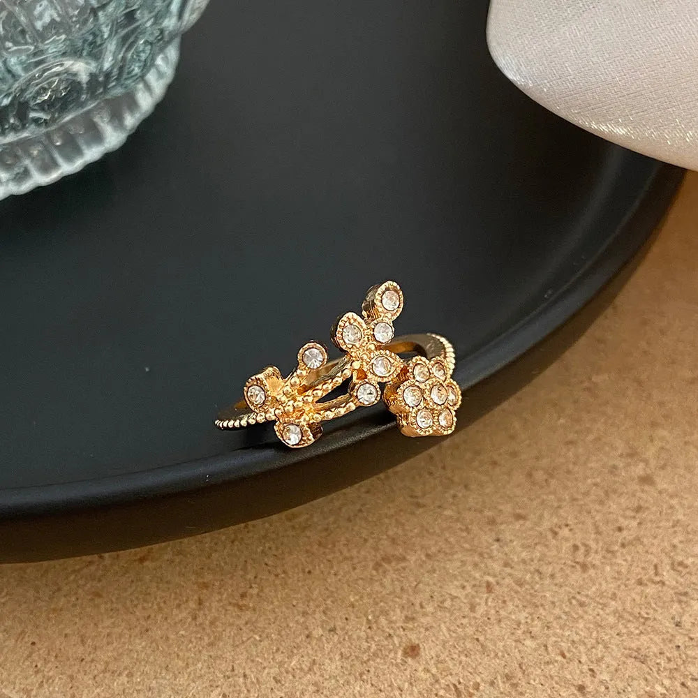 Women's open ring made of copper with a diamond finish, shaped as a detailed flower with leaves, shown in gold and white colour options.