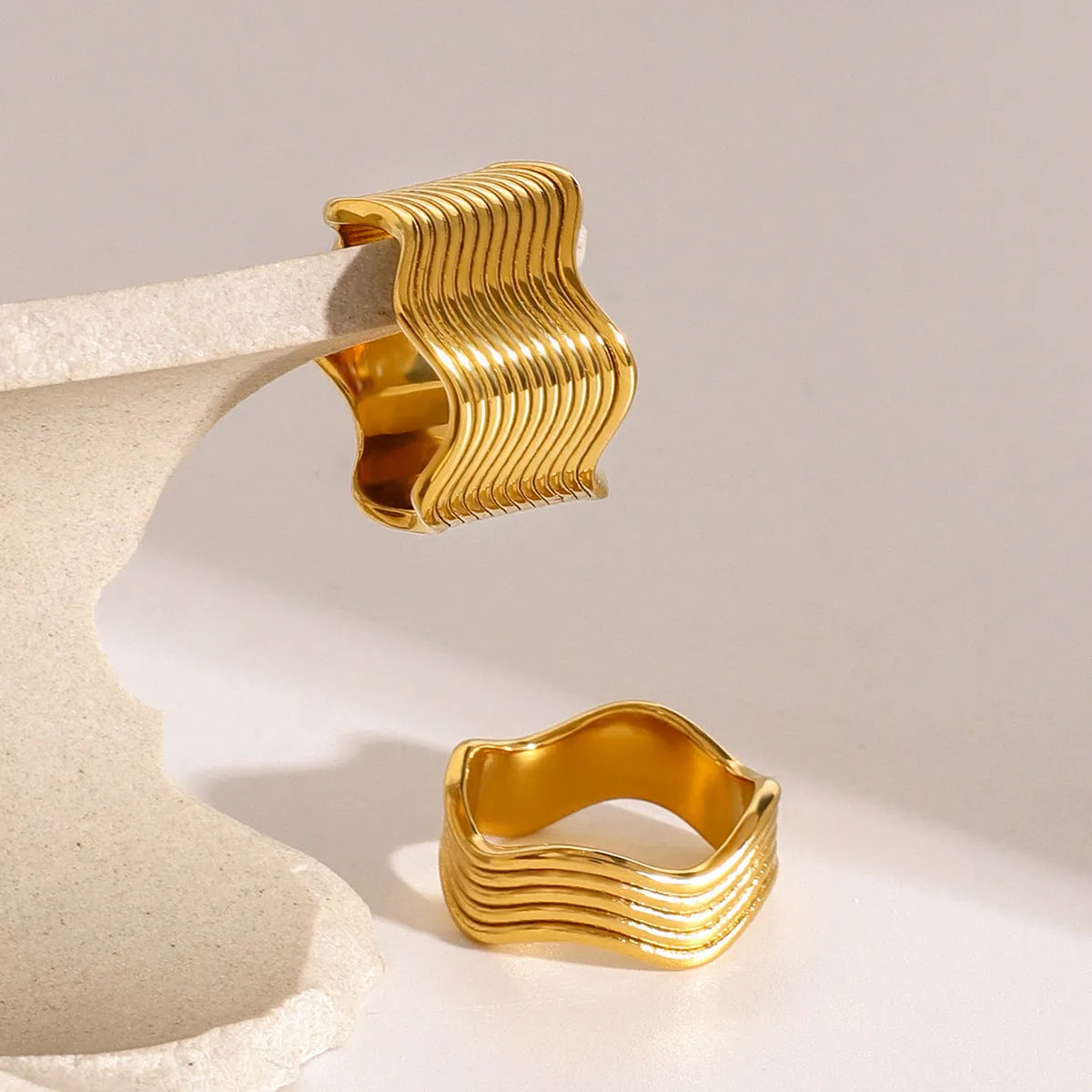 Stainless steel women's ring with a wide geometric wave surface design in a silver or gold finish.