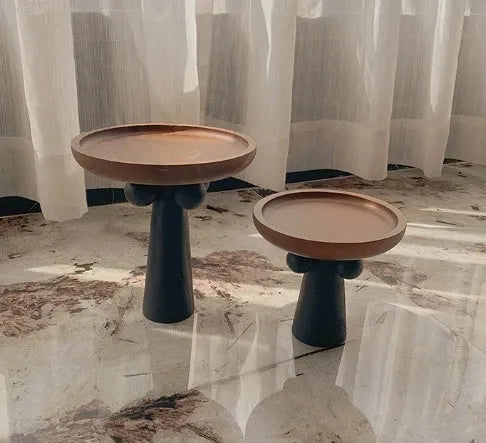 Round wooden tray with high Nordic-style legs in a light wood finish holding a candle