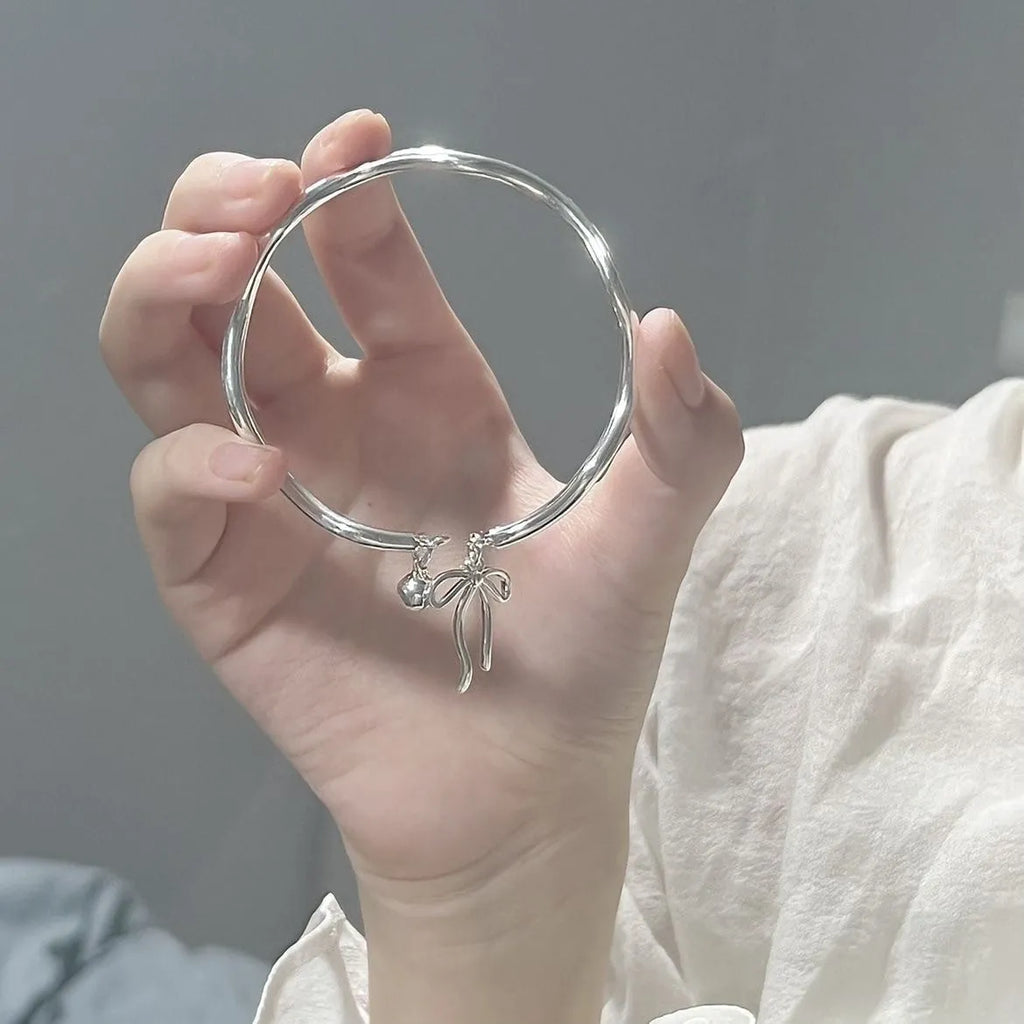 Silver adjustable bracelet with a detailed bow bell opening charm on a wrist.