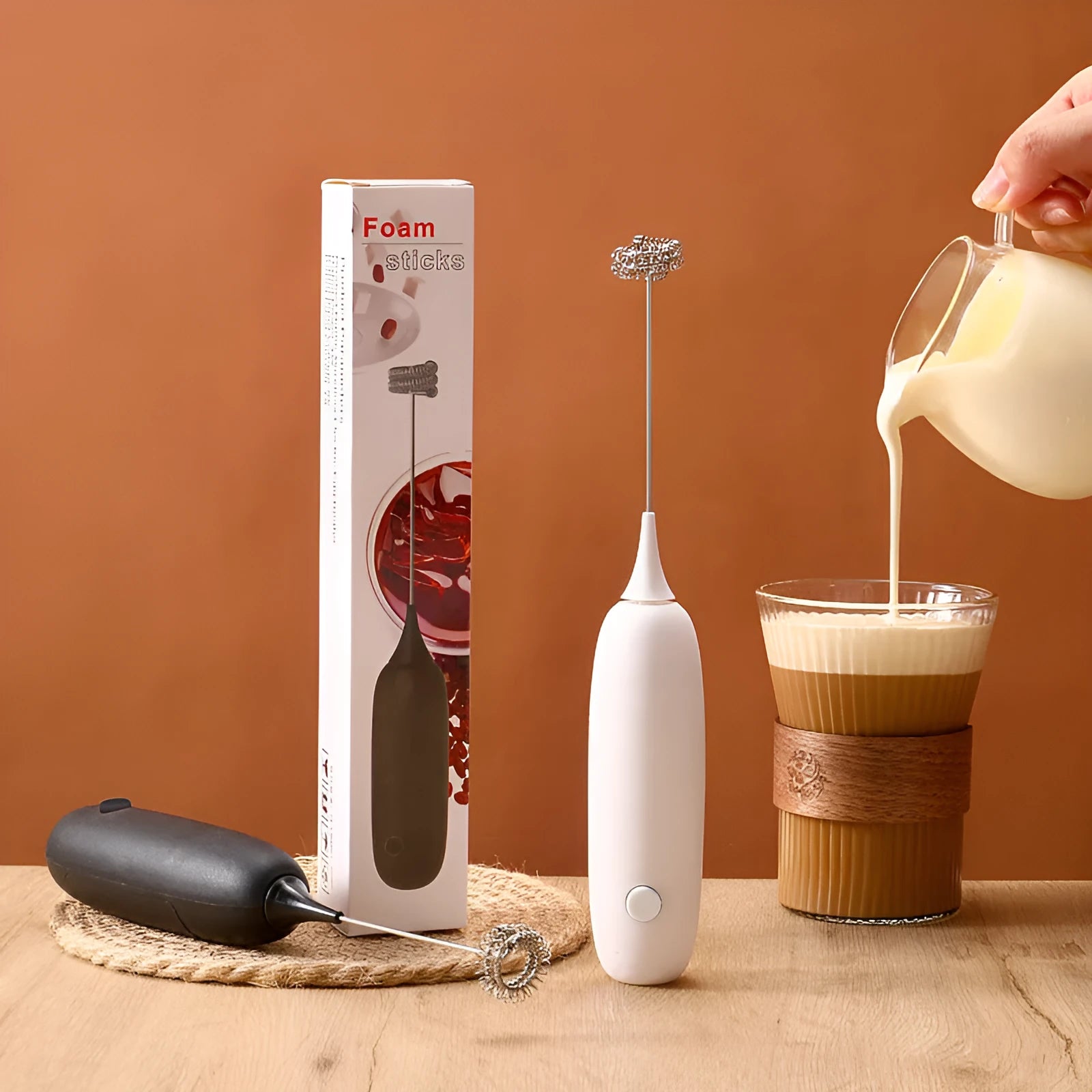 A hand-held electric milk frother in black and white colour options on a kitchen counter.