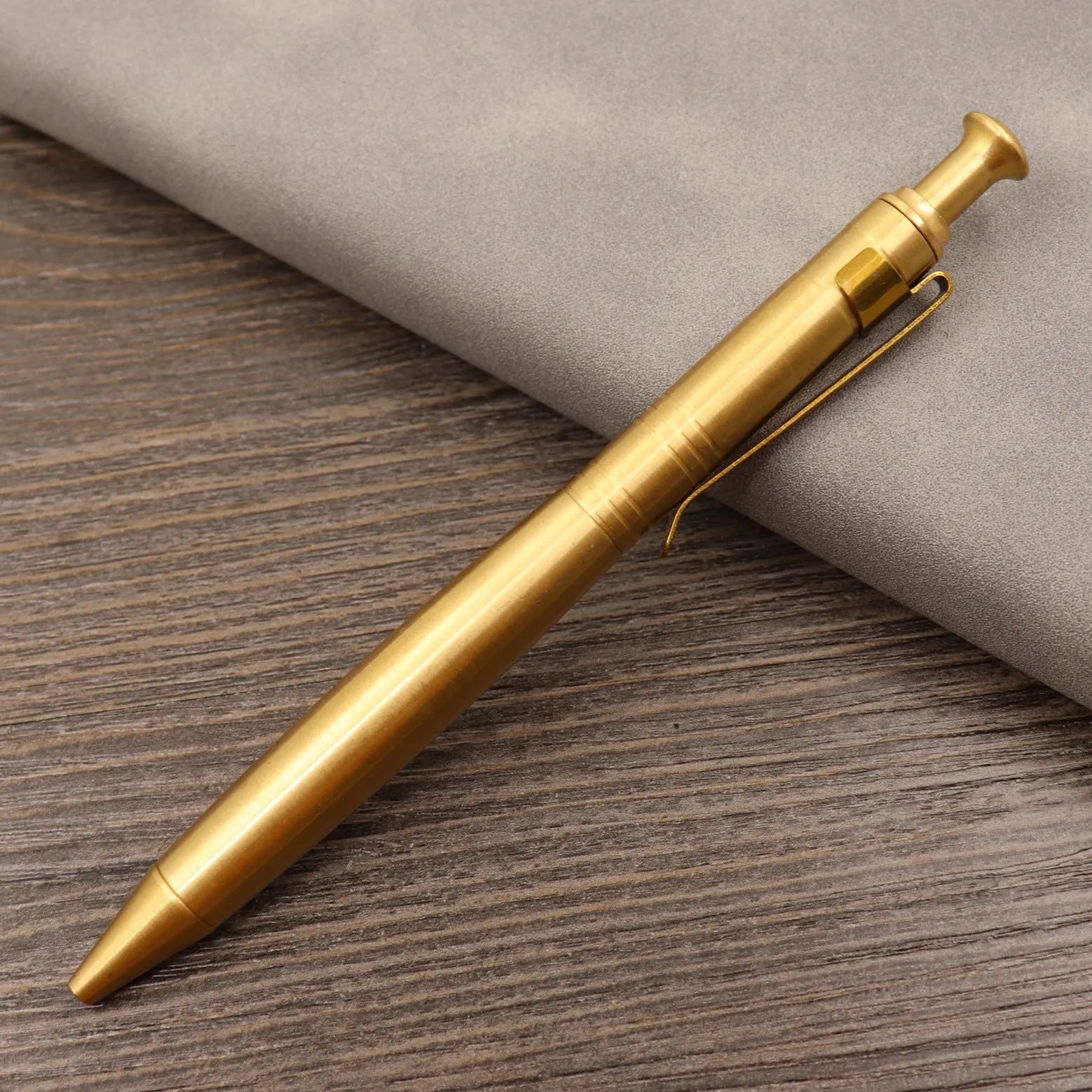 Brass bolt-action tactical pen in a retro copper finish, showing press mechanism and textured barrel.