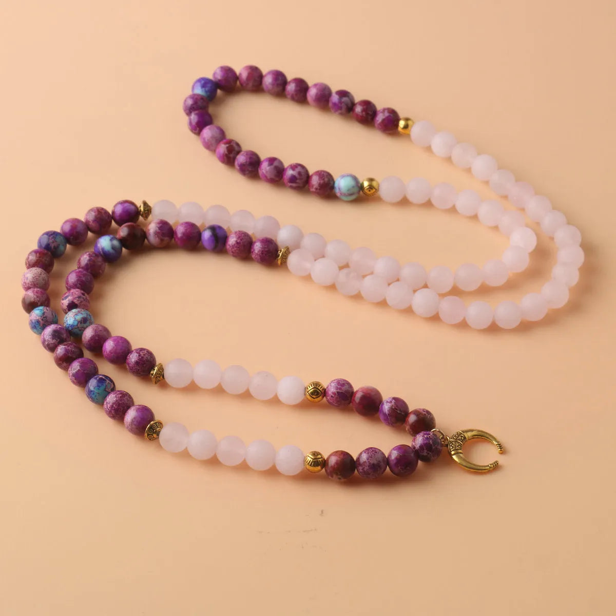 Round pink Emperor Stone pendant on a silver-tone chain, laid flat.