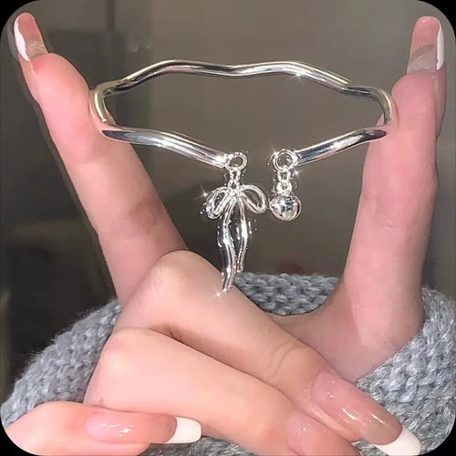 Silver adjustable bracelet with a detailed bow bell opening charm on a wrist.