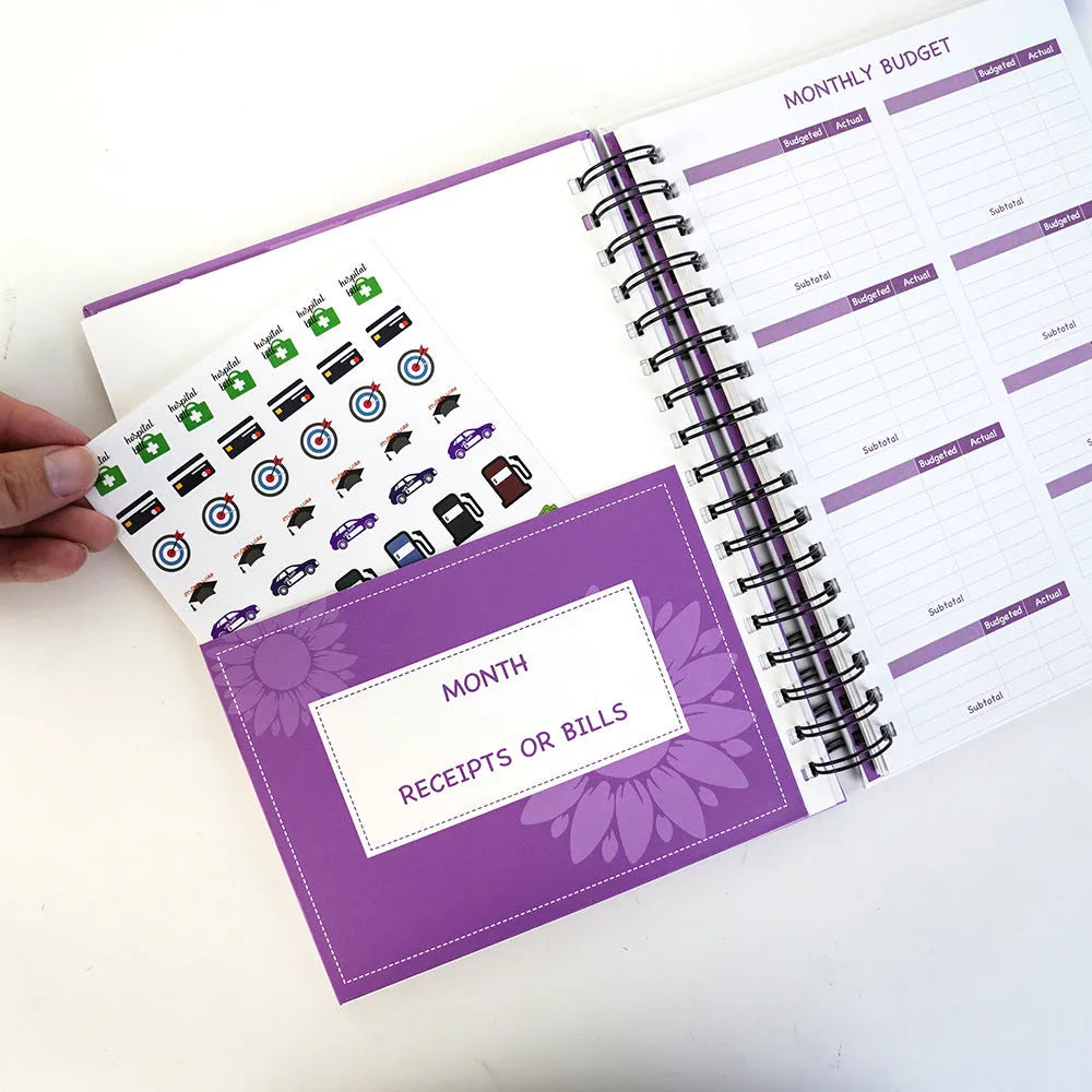 Purple coil-bound budget notebook with daolin paper pages, pen, stickers, and paper clips for financial planning