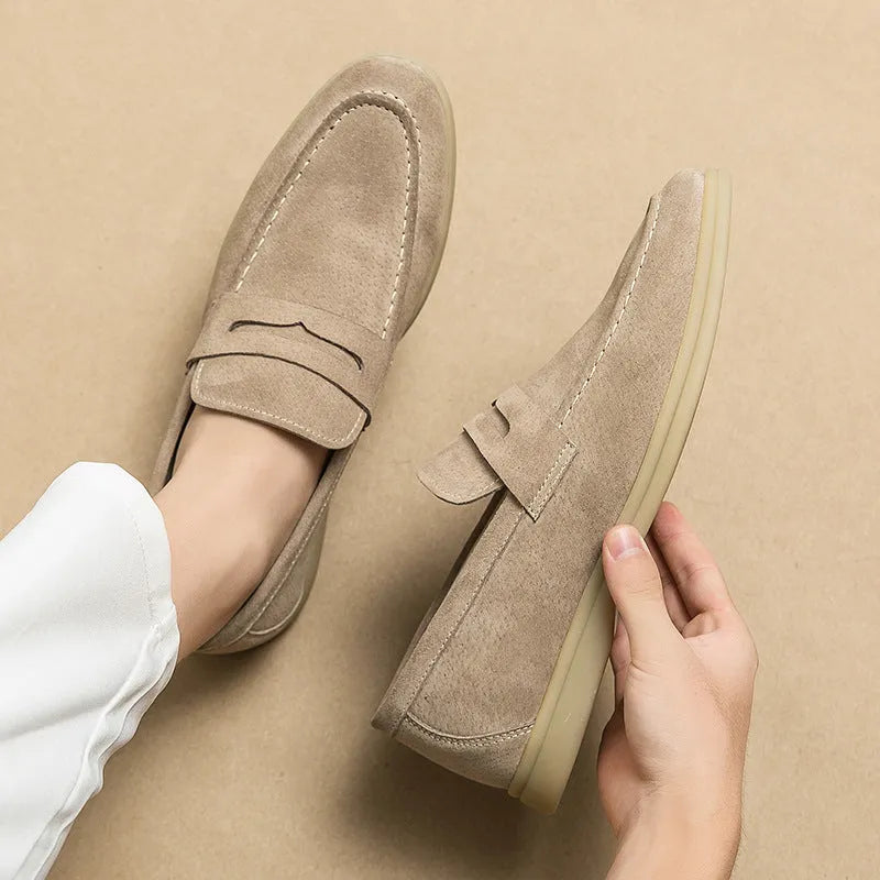 Men's brown leather slip-on casual shoes with round toe and rubber sole on a wooden floor.