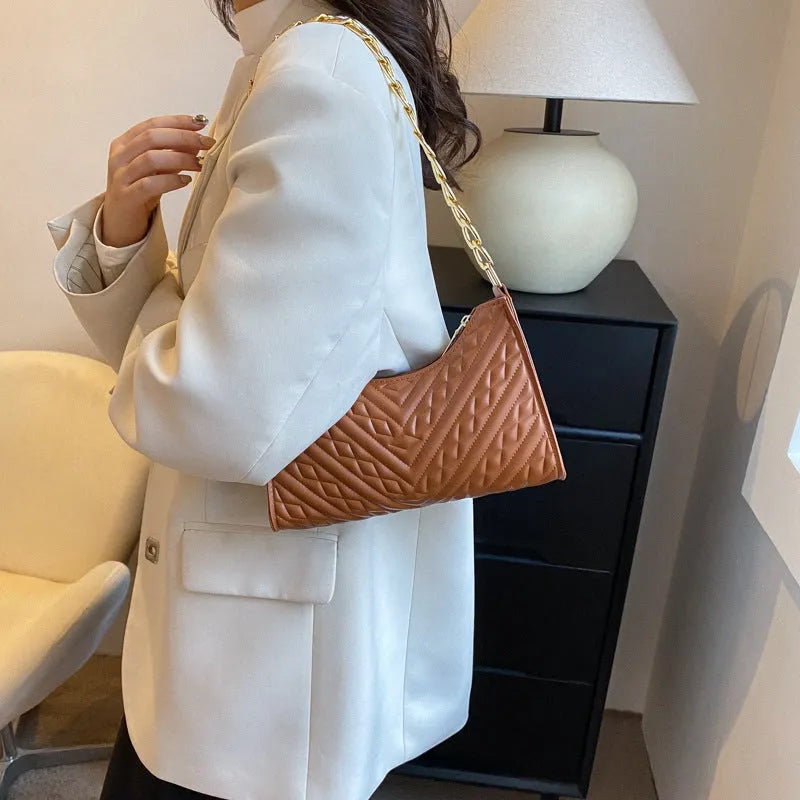 Vertical square brown PU shoulder bag with chain strap and soft handle on a table
