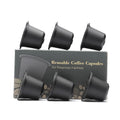 Six reusable black plastic coffee capsule filter cups with a spoon on a table