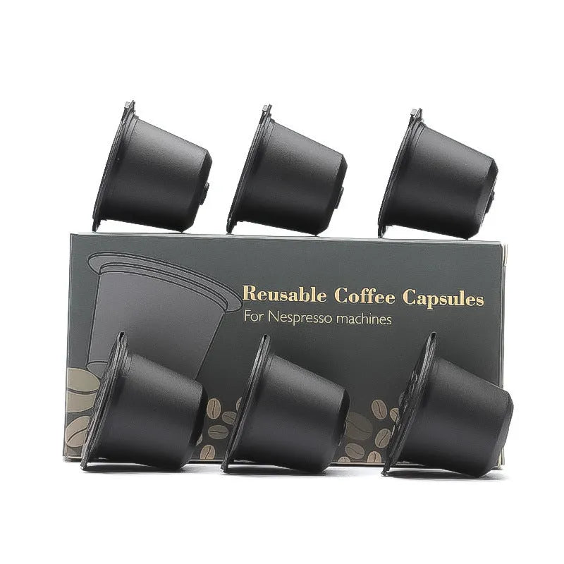 Six reusable black plastic coffee capsule filter cups with a spoon on a table