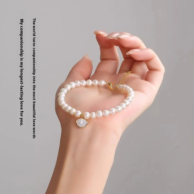 Women's freshwater pearl bracelet with central fan shell design on a wrist, showing elastic and chain fastening options.