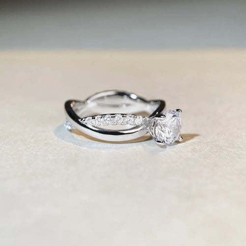 A geometric silver ring with a twisted band and a 1 carat moissanite stone in a four-claw setting.