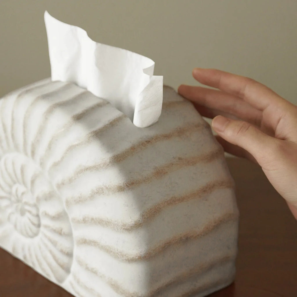 Solid resin conch-shaped tissue box cover in a natural colour on a table.