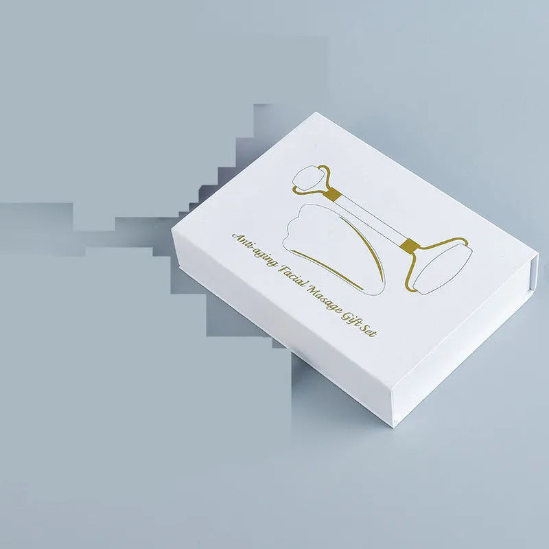 White jade double-headed facial roller and scraping board set on a plain surface.