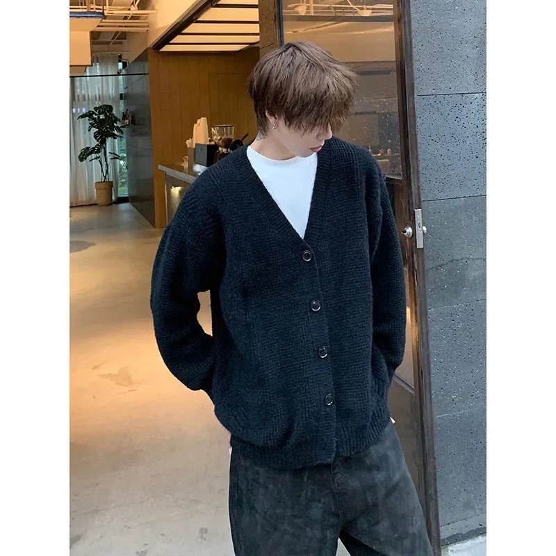 A man's loose-fitting V-neck knitted cardigan in a solid colour on a hanger.