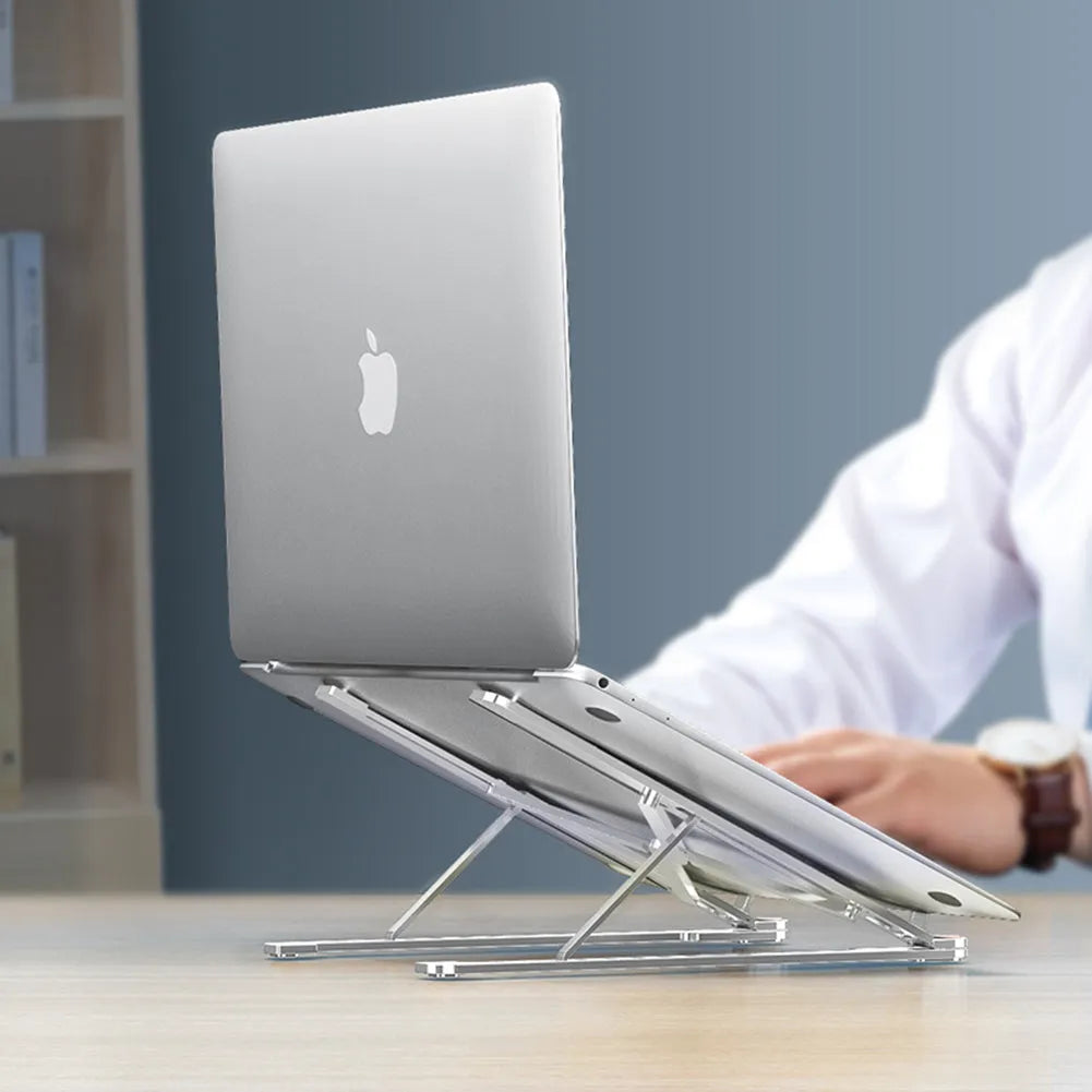 A folded silver aluminium laptop stand next to an open laptop, showing its thin profile and adjustable angle mechanism.