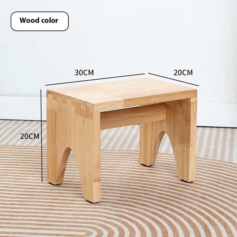 Solid wood distressed finish shoe changing stool with bracket legs in a living room setting.