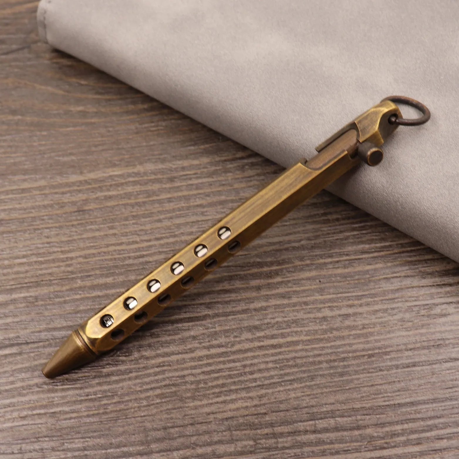 Brass bolt-action tactical pen in a retro copper finish, showing press mechanism and textured barrel.