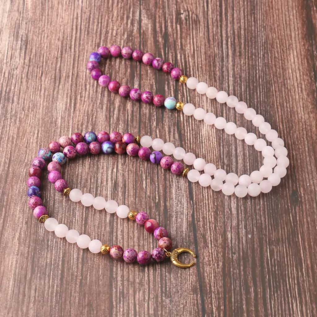 Round pink Emperor Stone pendant on a silver-tone chain, laid flat.