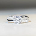A geometric silver ring with a twisted band and a 1 carat moissanite stone in a four-claw setting.