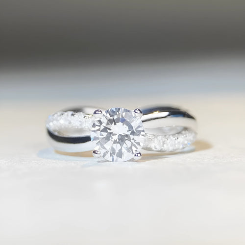 A geometric silver ring with a twisted band and a 1 carat moissanite stone in a four-claw setting.