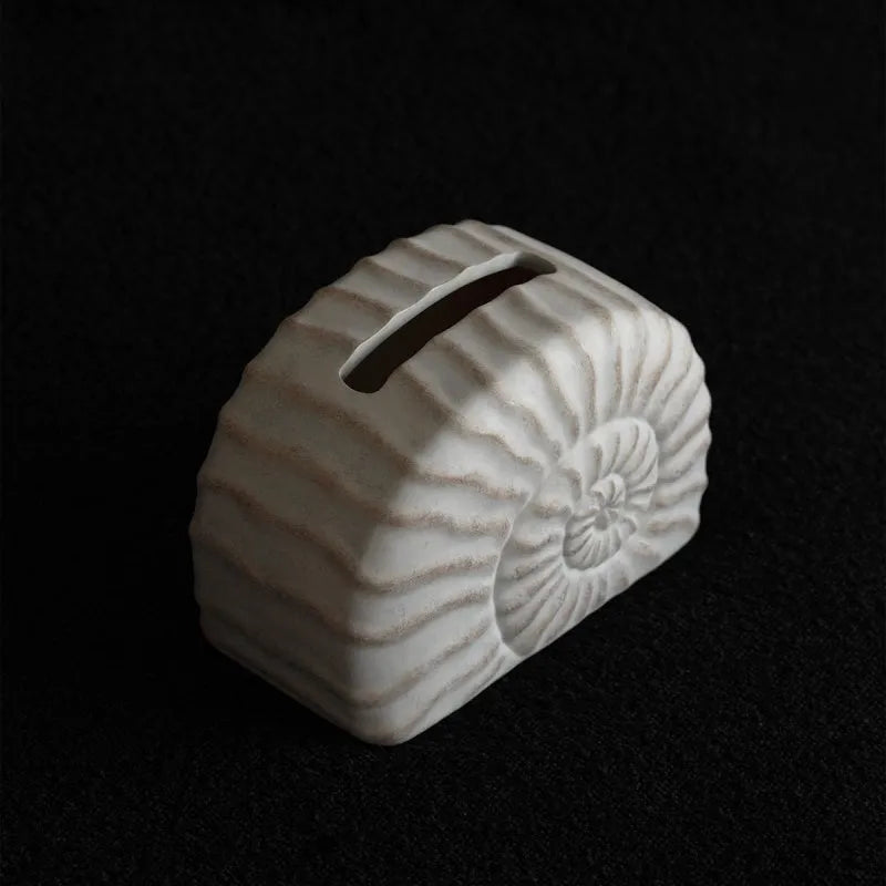 Solid resin conch-shaped tissue box cover in a natural colour on a table.