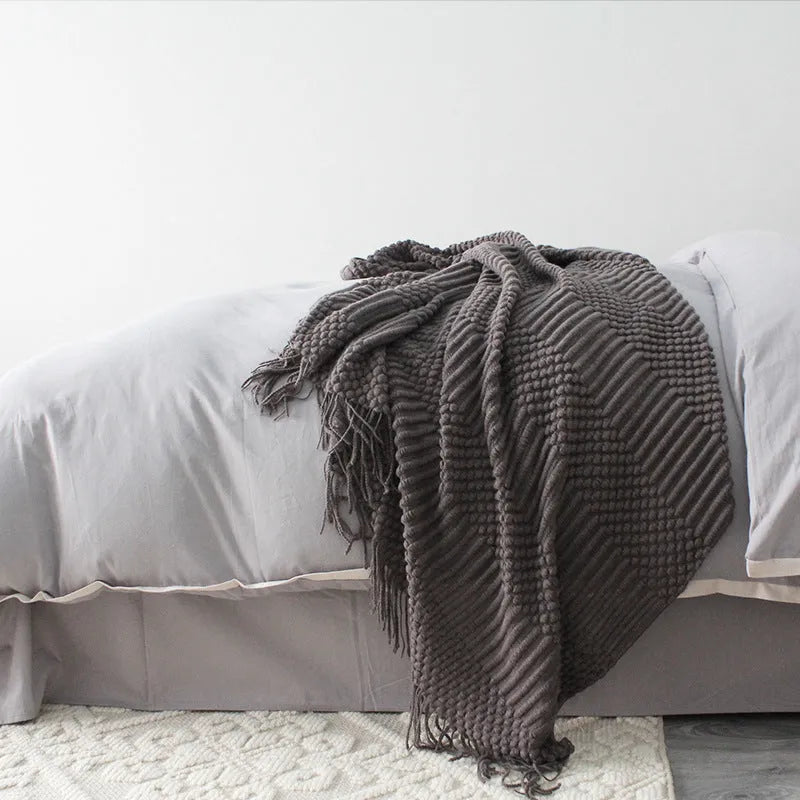 Small grey polyester nap blanket folded on a sofa, showing its texture and size.