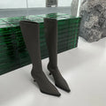 Black pointed toe knee-high boots with a stiletto heel and back zipper, shown on a model