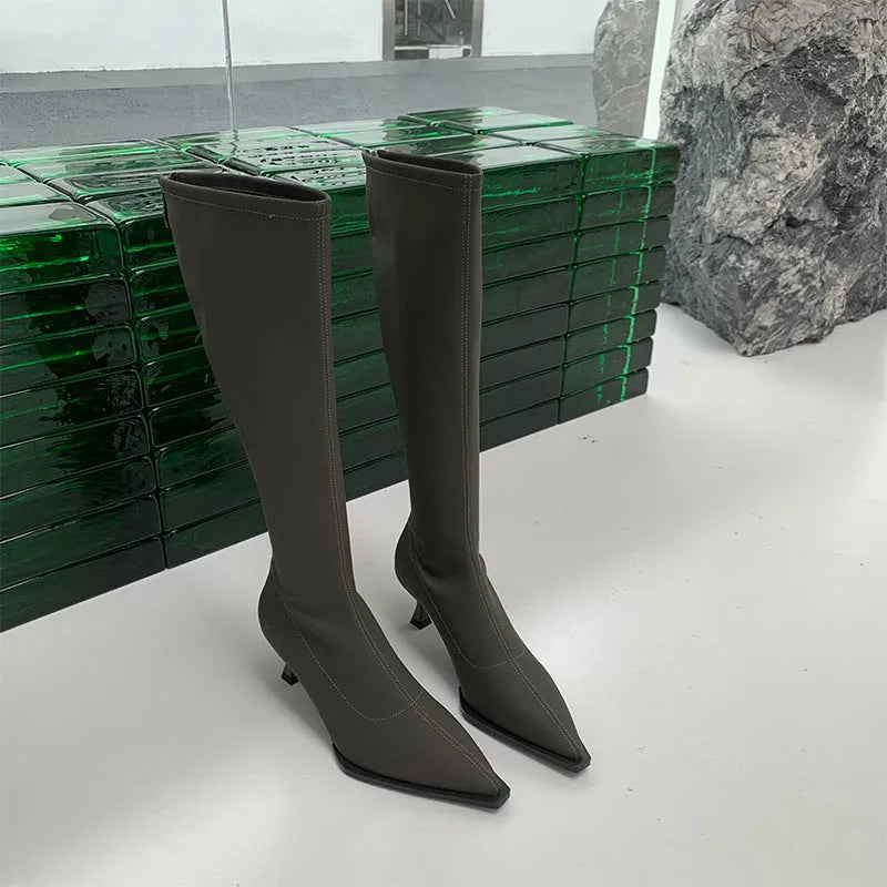 Black pointed toe knee-high boots with a stiletto heel and back zipper, shown on a model