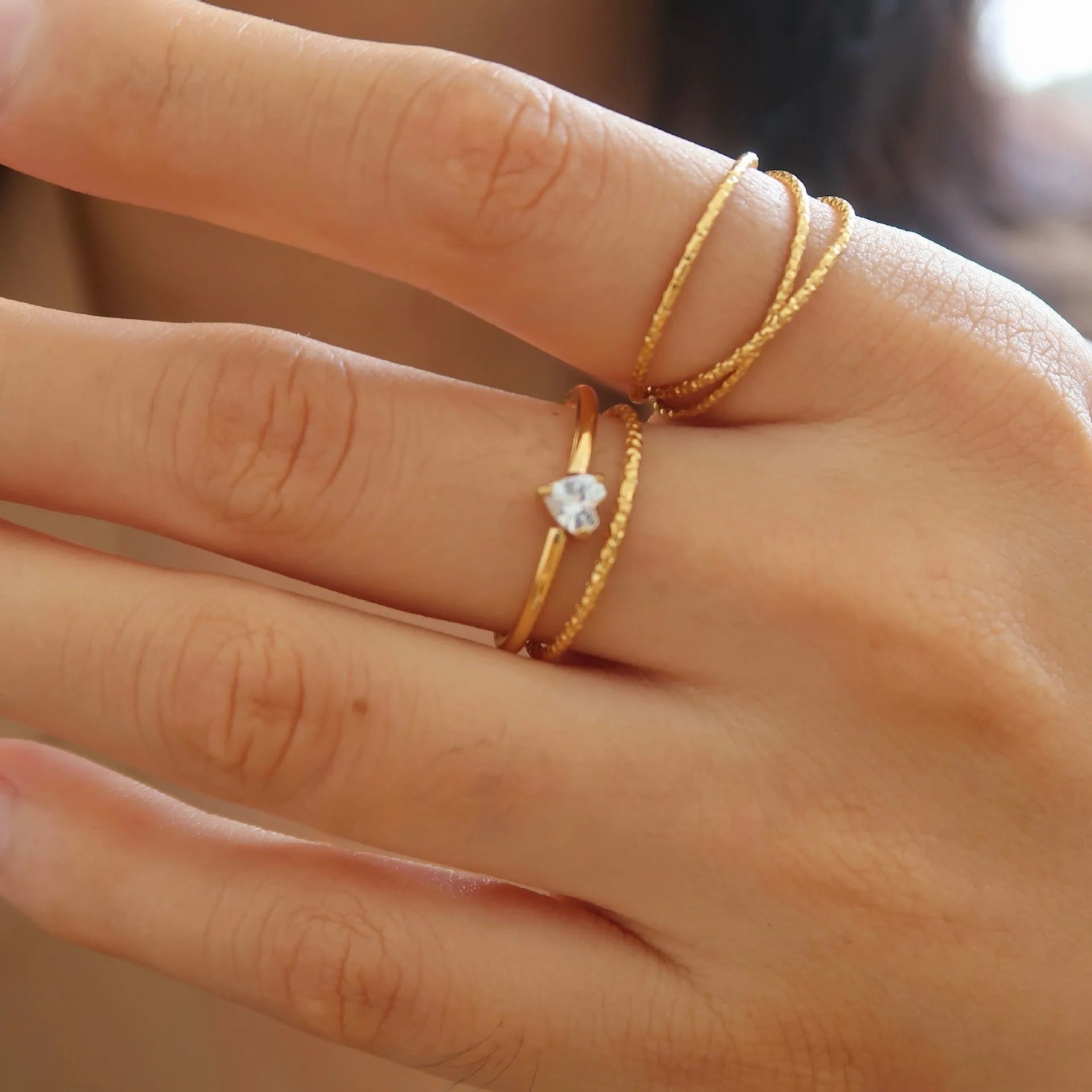 Golden electroplated stainless steel ring showing heart and oval shape designs on a hand.