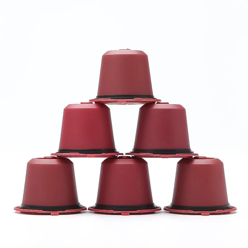 Six reusable black plastic coffee capsule filter cups with a spoon on a table