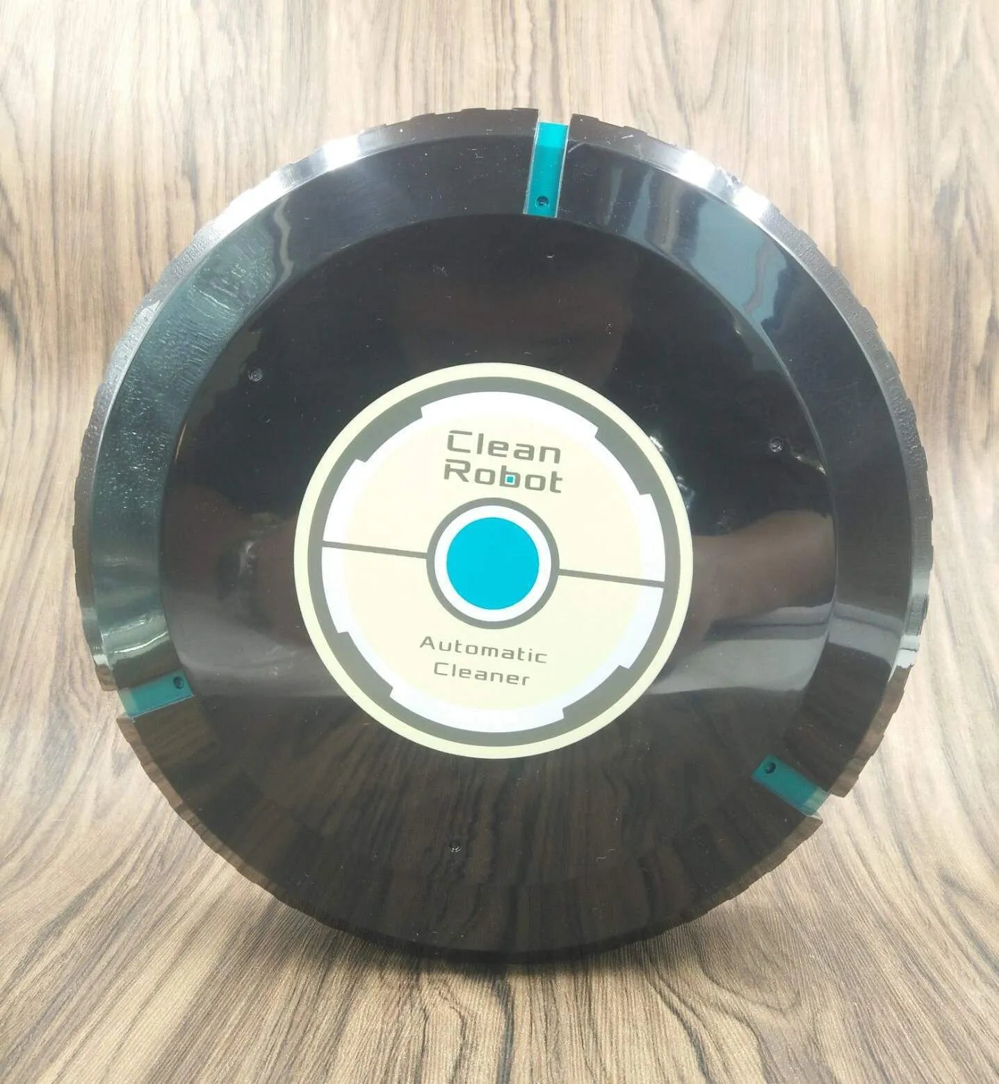 Black AC automatic sweeping robot vacuum cleaner on a wooden floor.