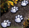 Set of four black bear paw print solar LED garden lights with a central solar panel pole on grass.