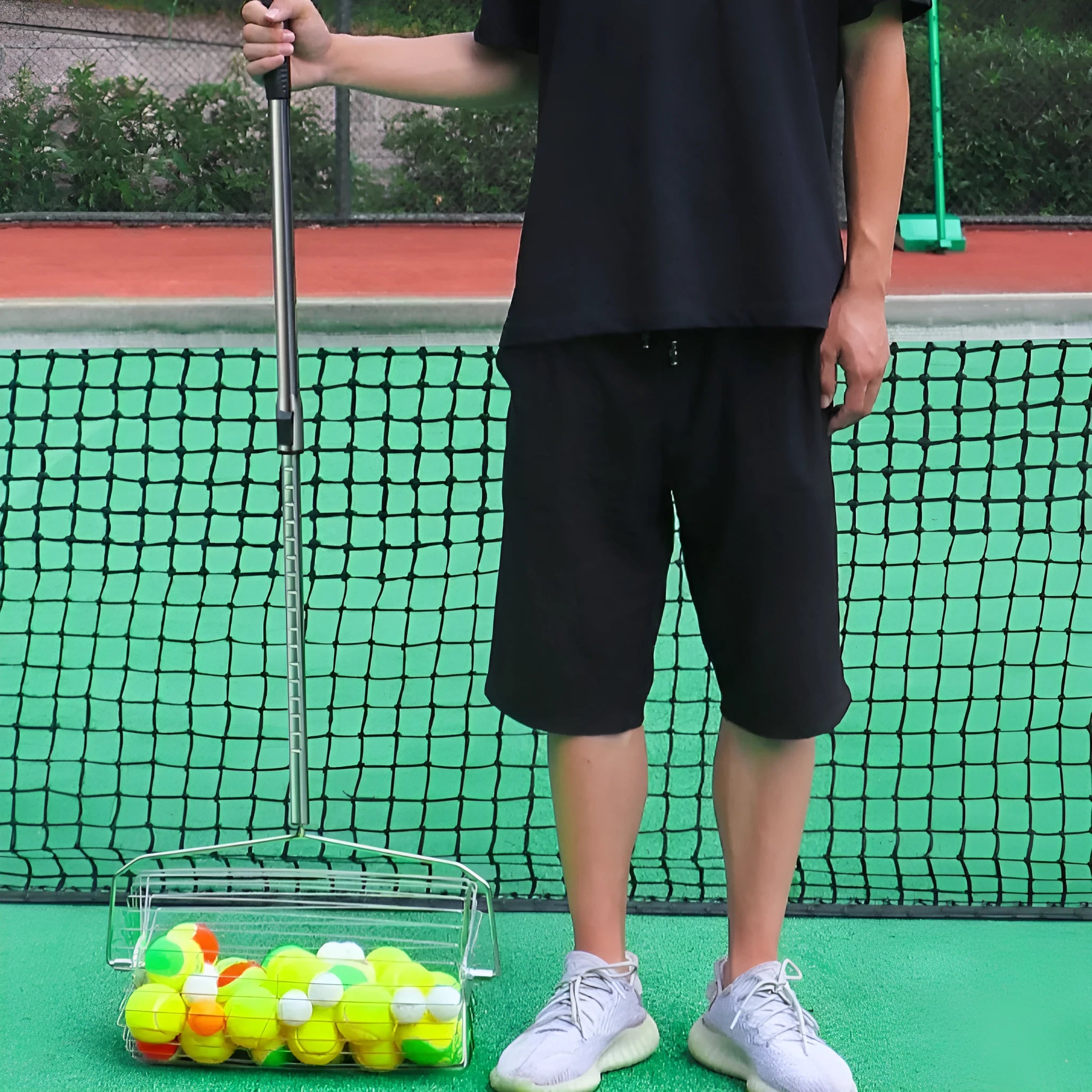 Stainless steel tennis ball roller picker with adjustable handle on a court.