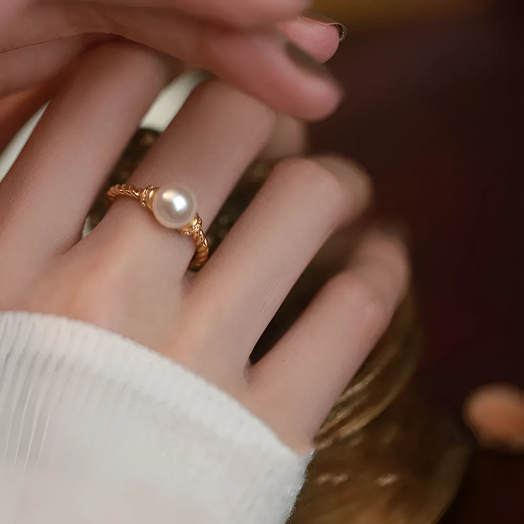 Adjustable geometric twist copper ring with a central pearl, shown in gold and silver colour options.
