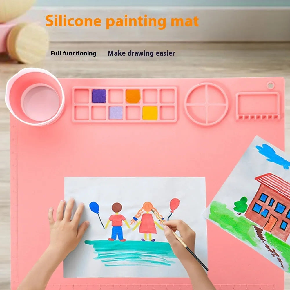 Light blue silicone painting mat with an integrated bowl on one side, positioned on a wooden table.