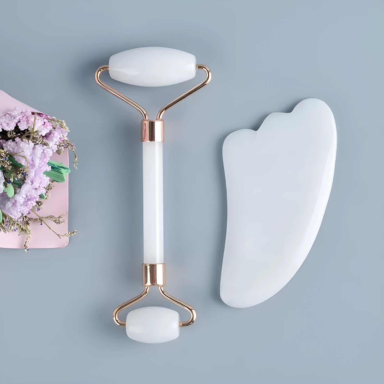 White jade double-headed facial roller and scraping board set on a plain surface.