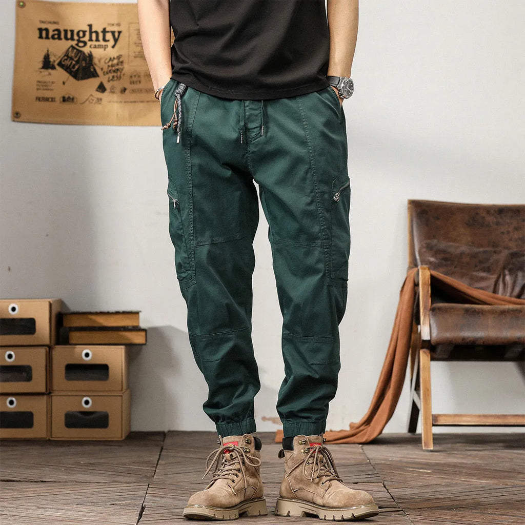 Men's khaki cotton tapered harem pants with ankle bands and a zip fly, laid flat.