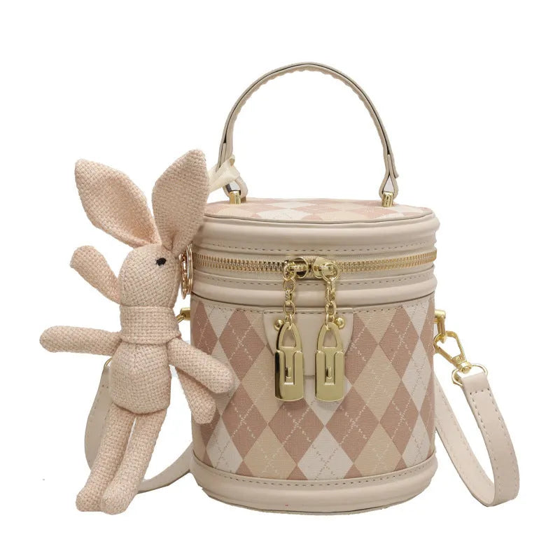 Textured rhombus cylindrical PU bucket bag in beige with white rabbit pendant, 14 cm wide.