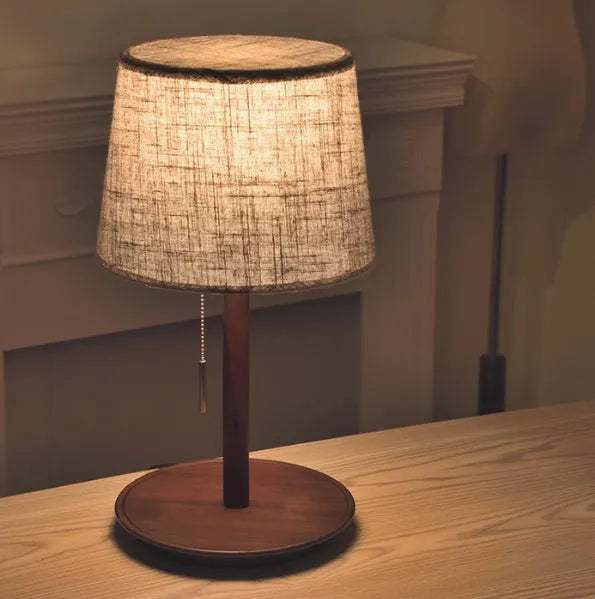 Walnut coloured solid wood table lamp with white cloth lampshade and black cable switch.